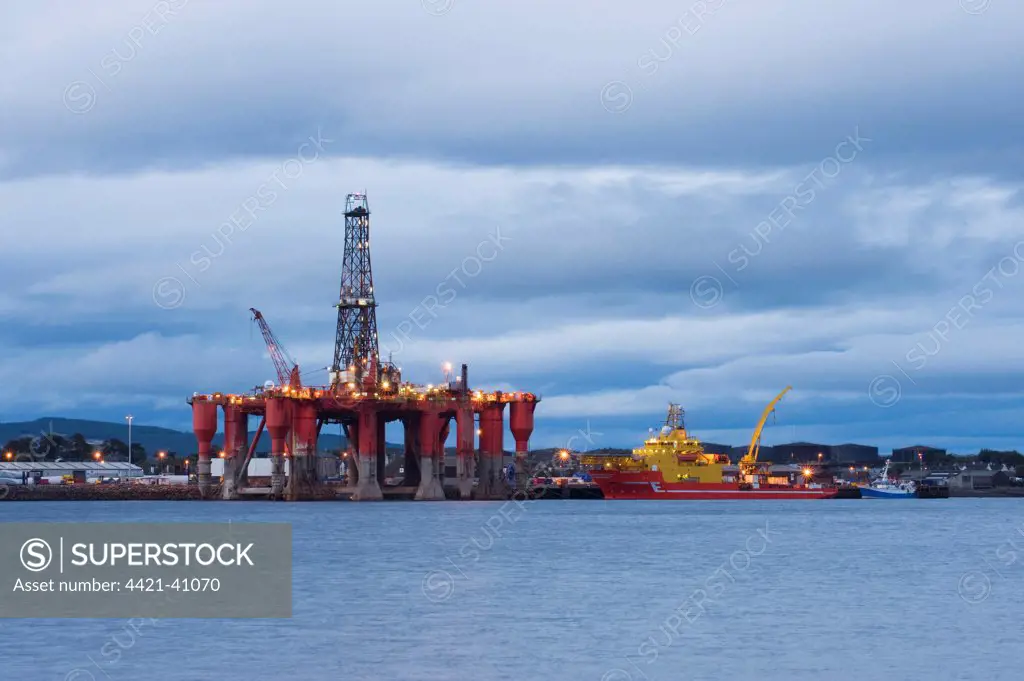 Oil rig moored in sea near coast at dusk, with offshore support vessel, Cromarty Firth, Moray Firth, Invergordon, Easter Ross, Scotland