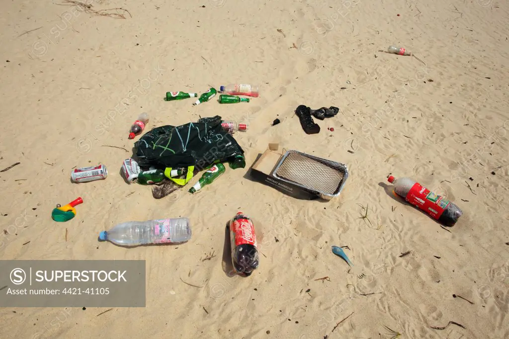 Plastic and glass bottles, plastic bag, disposable barbeque and bong, litter on sandy beach, Studland, Dorset, England, may