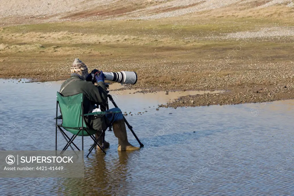 Bird photographer sitting in chair, waiting in coastal pool, Salthouse, Norfolk, England, february