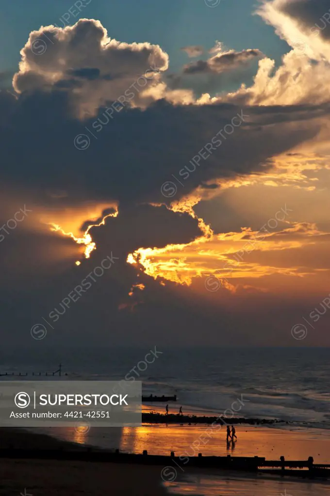 View of people on beach, groynes and clouds at sunset, Cromer, Norfolk, England, July