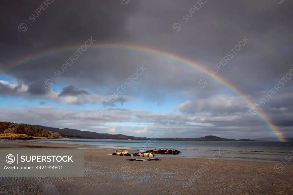 Bay of small Isles on the Isle of Jura, looking north,  with rainbow arcing from the mainland on the left over Knockrome .low tide.