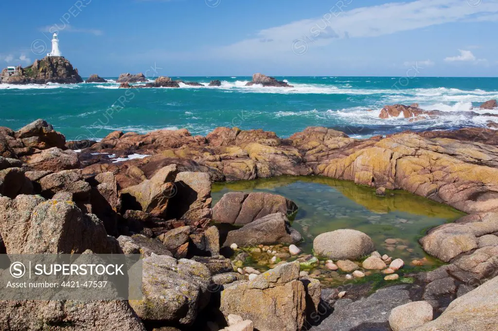 Rockpool on rocky shore at low tide, with lighthouse in background, La Corbiere Lighthouse, La Corbiere, St. Brelade, Jersey, Channel Islands, May