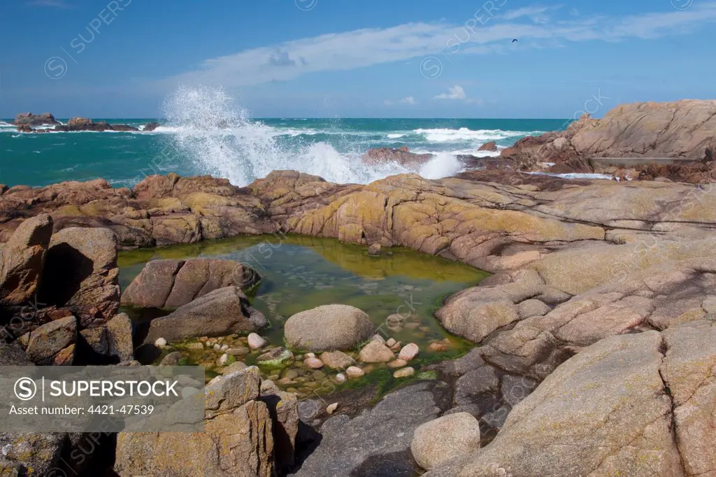 Rockpool and waves on rocky shore at low tide, Jersey, Channel Islands, May