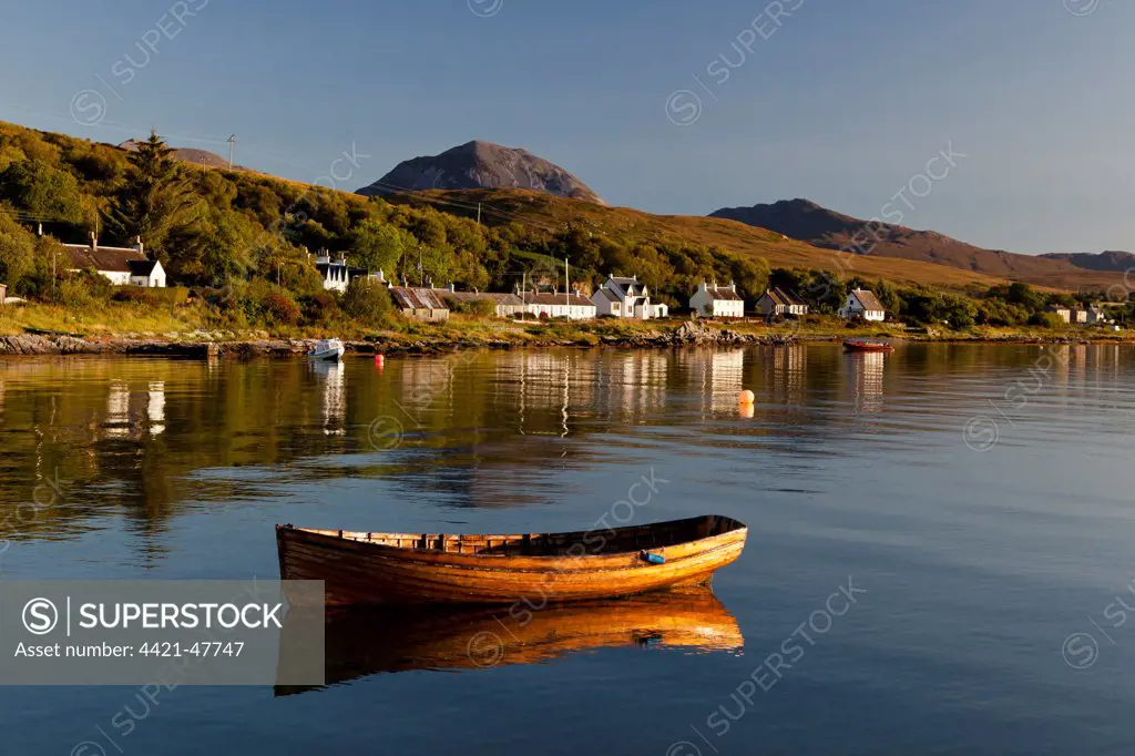 View of small wooden boat and village houses in bay,  in morning sunlight, with Beinn Shiantaidh and Corra Bheinn, Paps of Jura in background, Craighouse, Isle of Jura, Inner Hebrides, Scotland