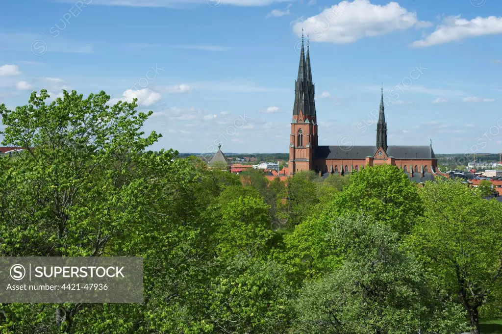View over trees towards city cathedral with spires, Uppsala Cathedral, Uppsala, Uppsala County, Uppland, Sweden, may