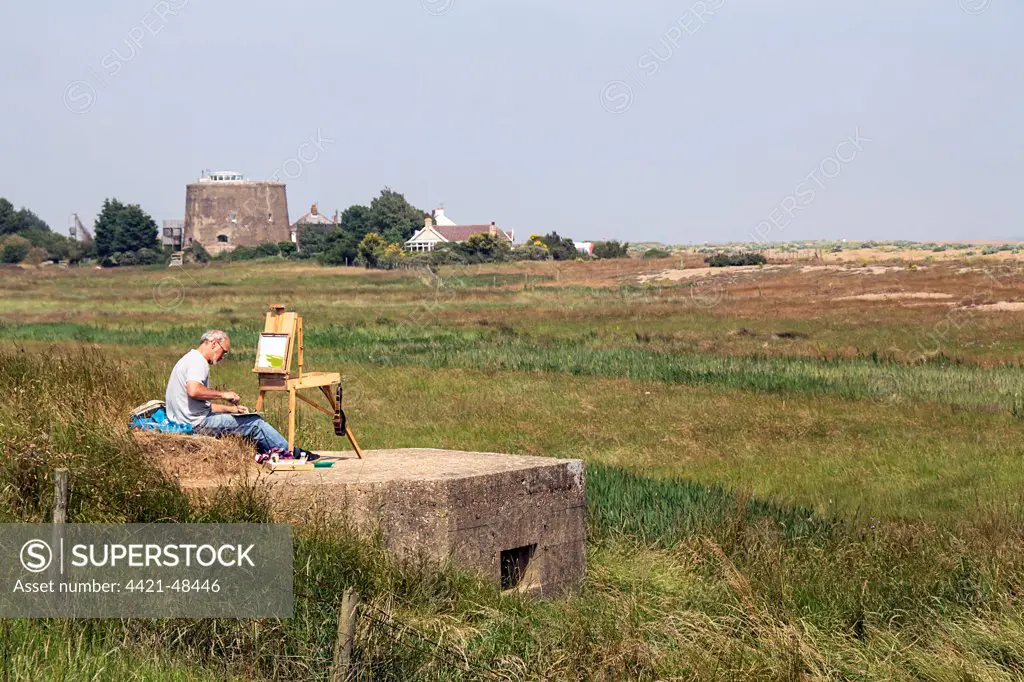 Artist sitting on World War 2 pill box looking over Oxley marsh at Shingle Street, Suffolk. Note the Martello Tower number AA.