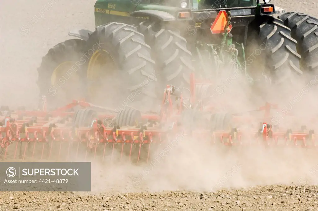 Close-up of tractor pulling harrows, harrowing field with wind blown dust, Sweden, spring