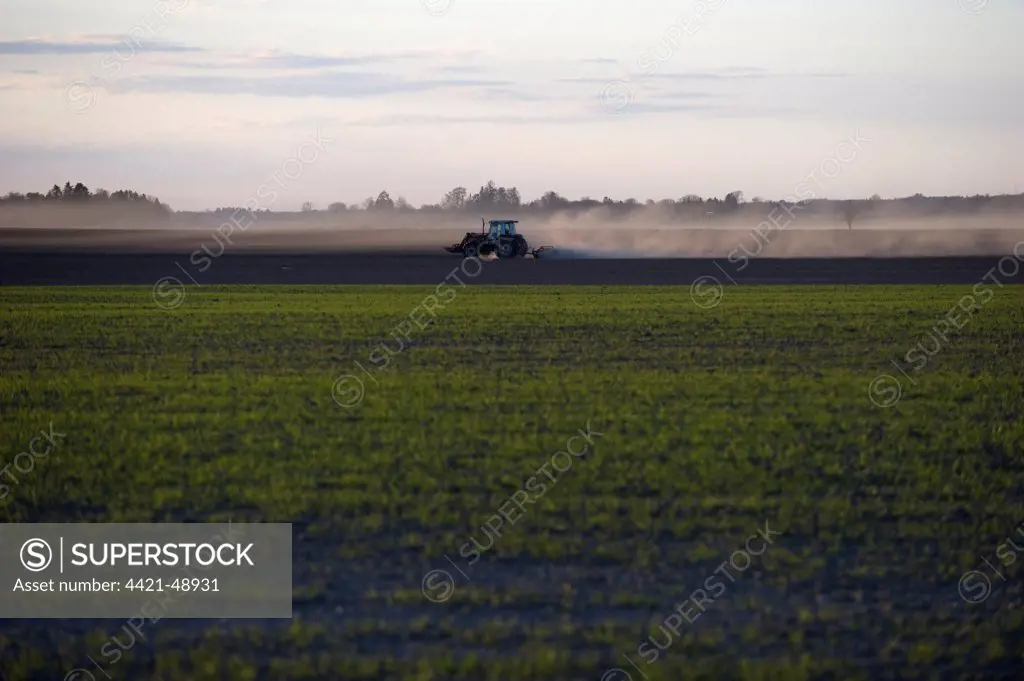 View across arable field, tractor with rollers, rolling field at sunset, Uppland, Sweden, may