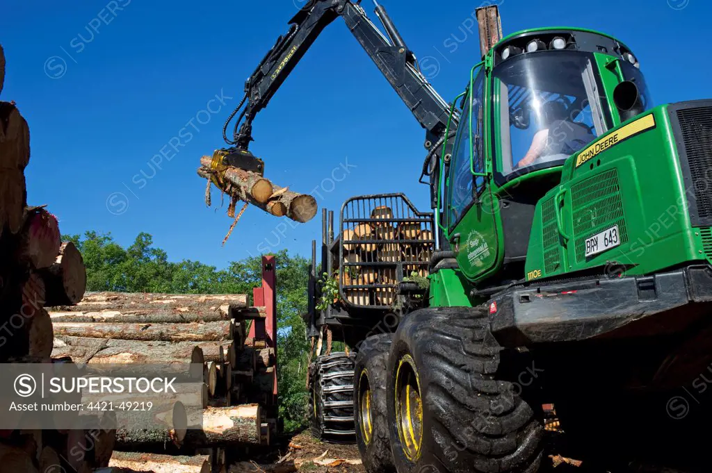 John Deere 1010E Forwarder loading logs onto timber barge, Archipelago Sea, Baltic Sea, Sweden, june