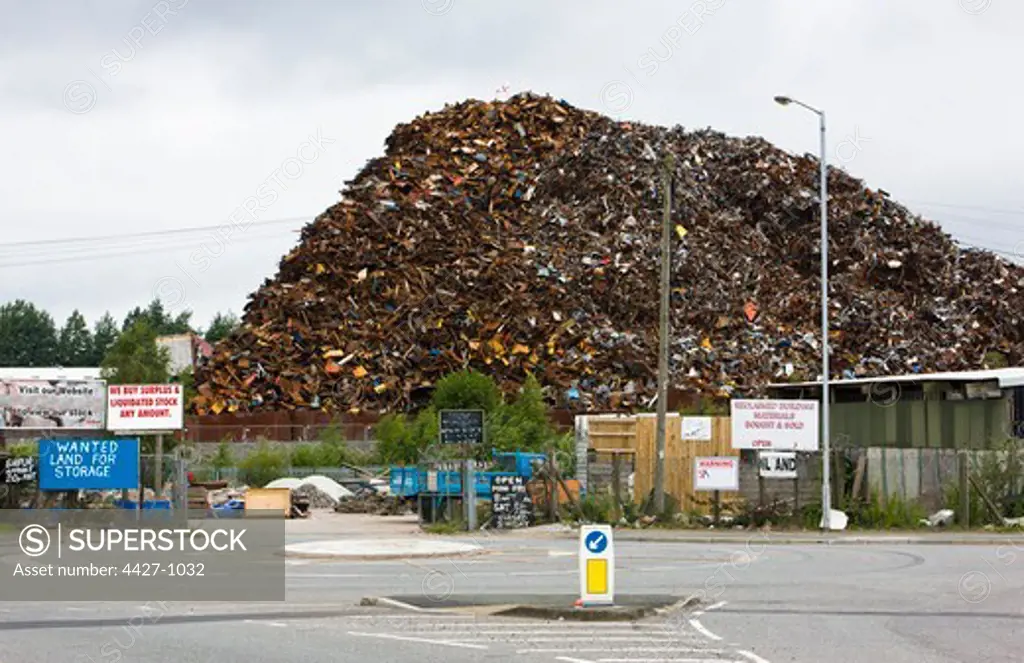 Large pile of scrap metal with signs on the public road in foreground, Widnes, Cheshire, England
