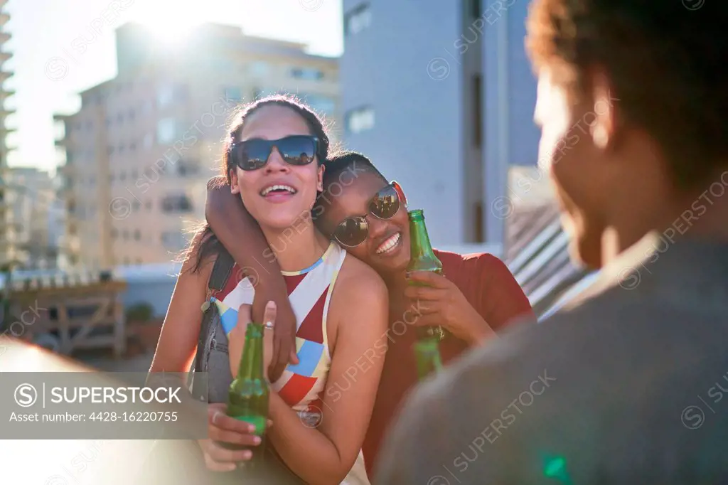 Happy young women friends drinking beer on sunny summer rooftop