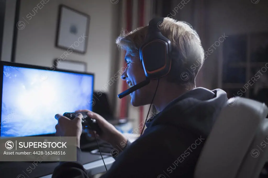 Happy teenage boy with headset playing video game at computer