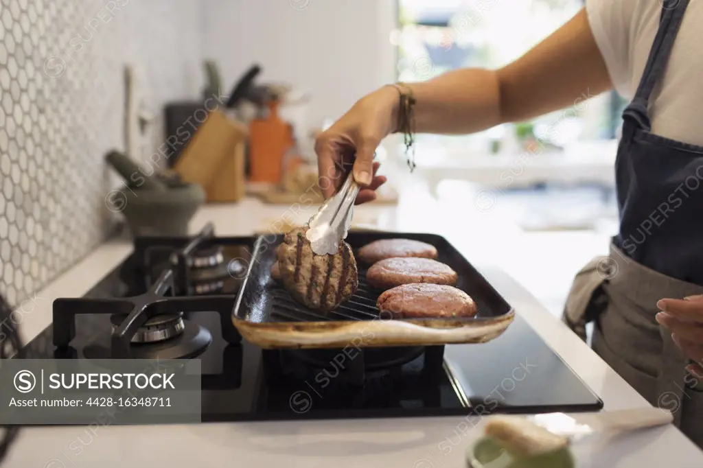Woman grilling hamburgers at kitchen stove