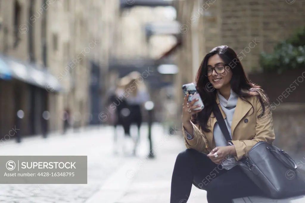 Smiling businesswoman using smart phone on city sidewalk