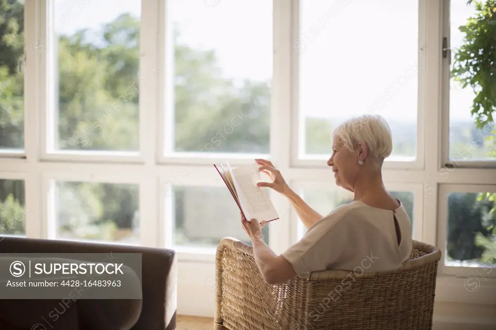 Senior woman relaxing and reading book in sunny living room