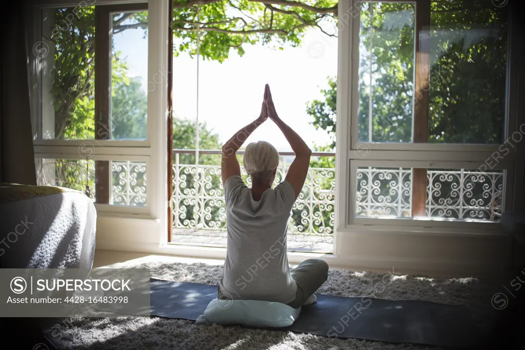Serene senior woman practicing yoga at sunny tranquil balcony doorway
