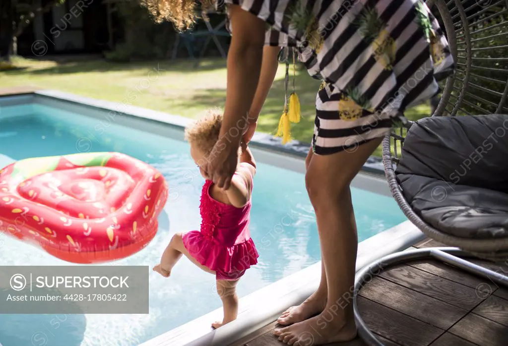 Mother helping toddler daughter at summer swimming pool