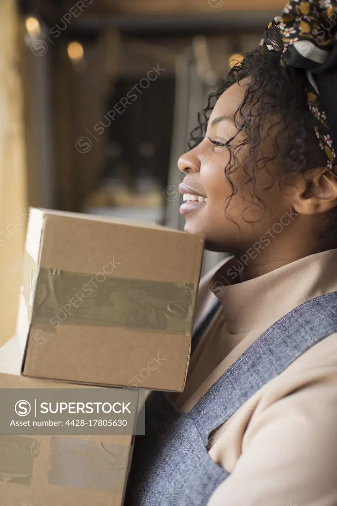 Happy female shop owner carrying stack of boxes