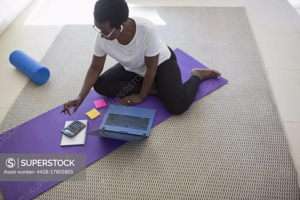 Mature woman paying bills and working at laptop on yoga mat