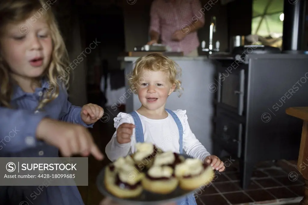 Cute girls reaching for biscuits with jelly and cream