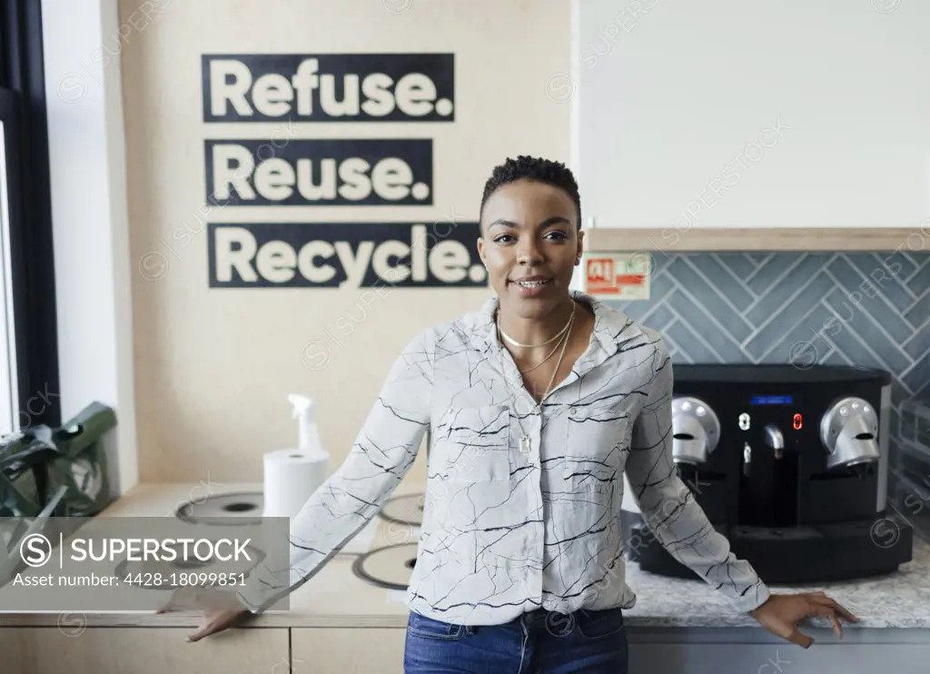 Portrait confident businesswoman at recycling bins in office kitchen