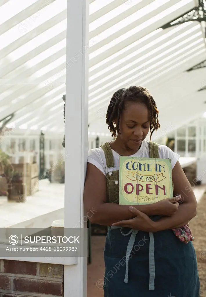 Female plant nursery owner with open sign in greenhouse doorway