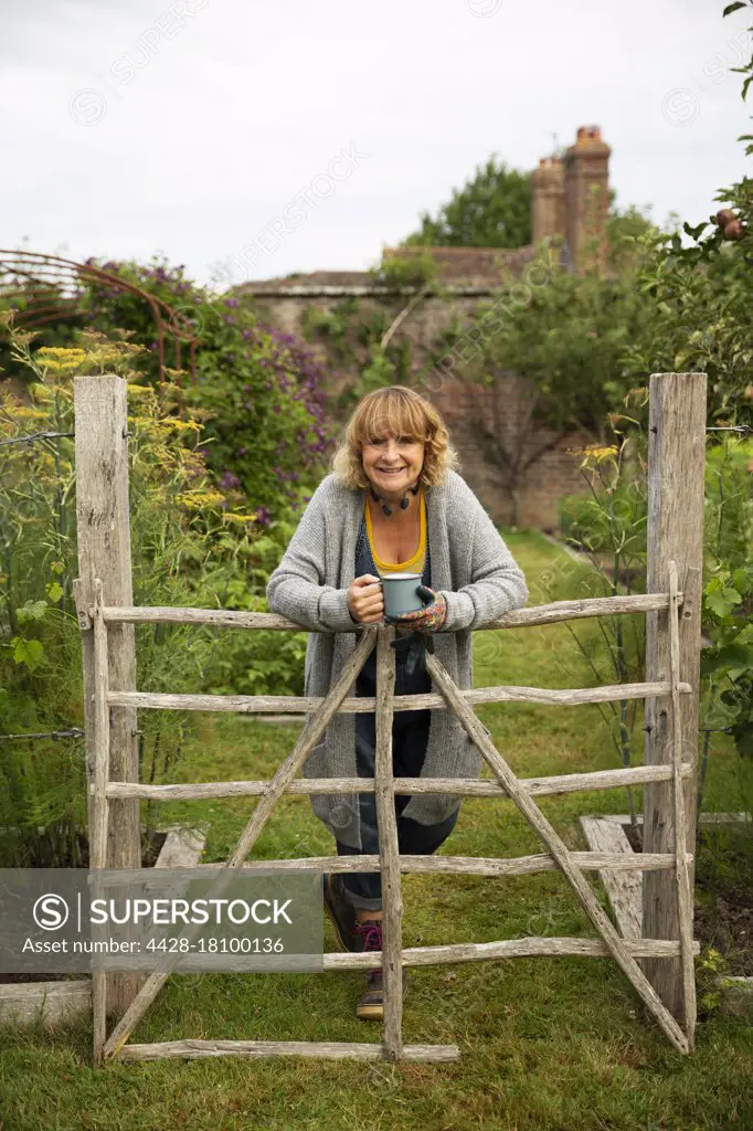 Portrait smiling woman drinking tea at gate in cottage garden