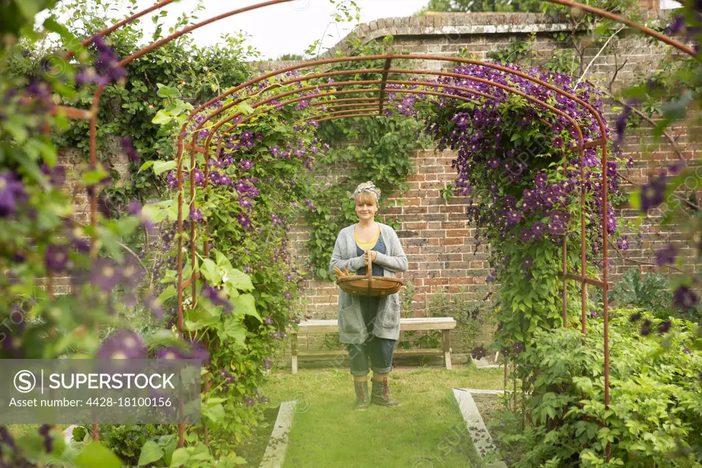 Portrait woman with basket under garden trellis with purple flowers