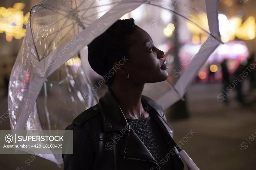 Serene young woman under umbrella on city sidewalk at night