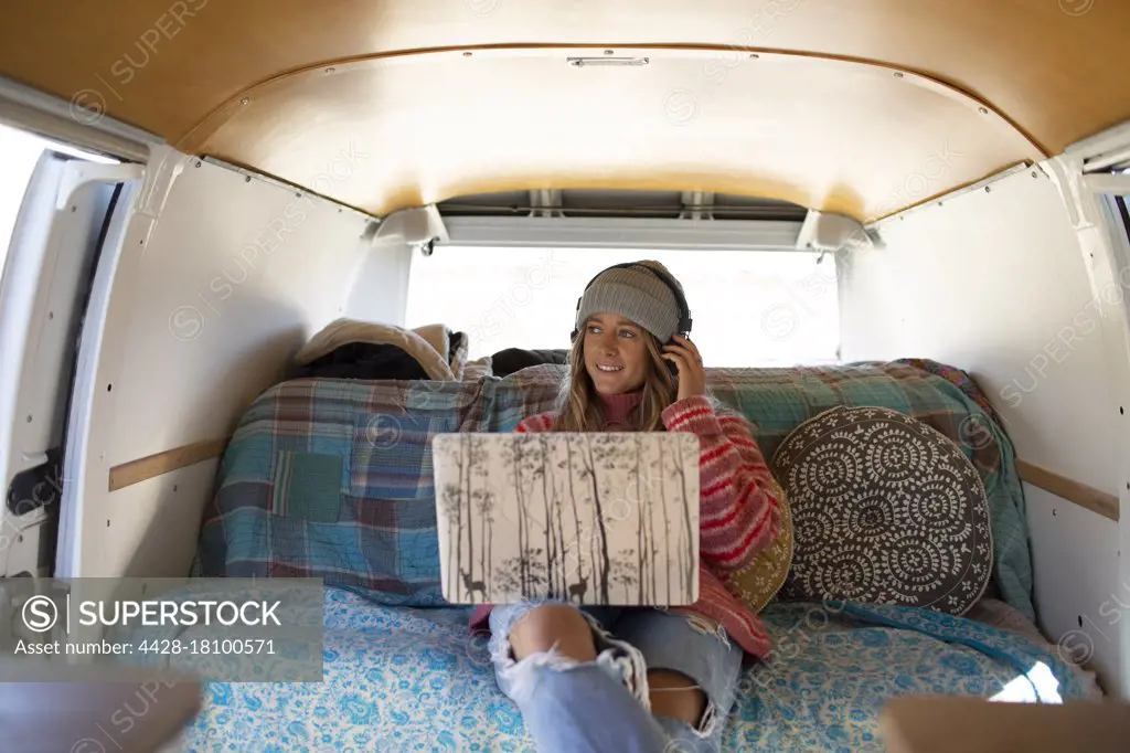 Carefree young woman with headphones and laptop in camper van
