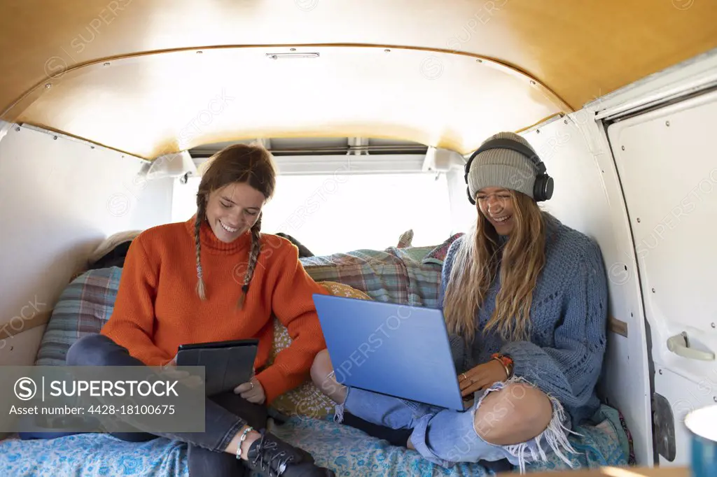 Young women friends relaxing with technology inside camper van