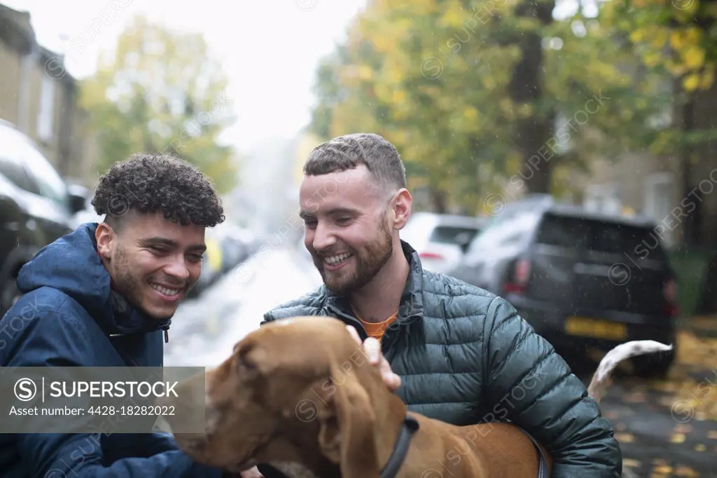 Happy gay male couple with dog on wet urban street