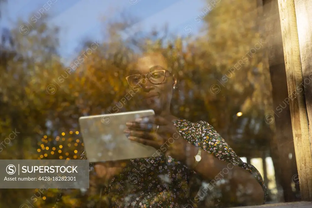 Woman using digital tablet at window with reflection of autumn trees