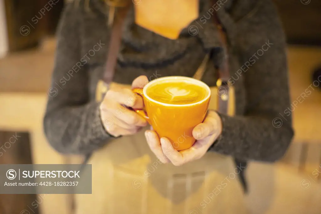 Close up female barista holding cappuccino with heart foam