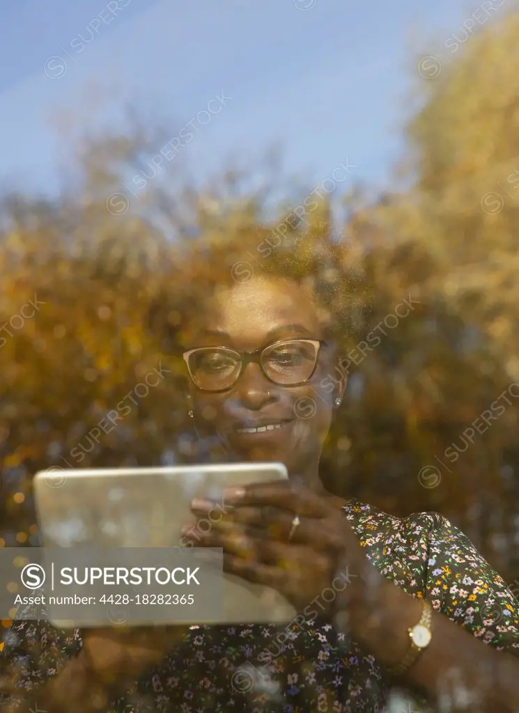 Smiling woman using digital tablet at sunny autumn window
