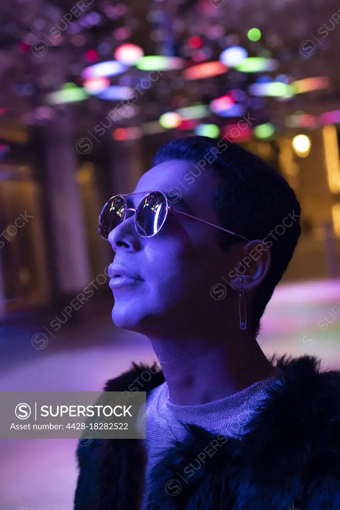 Portrait stylish young man in sunglasses looking up at neon lights