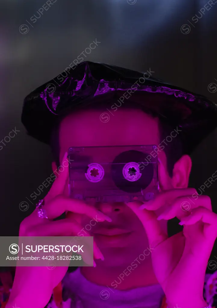 Portrait stylish young man holding cassette tape over face