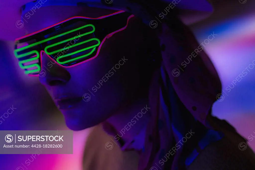 Close up stylish woman wearing neon sunglasses in dark