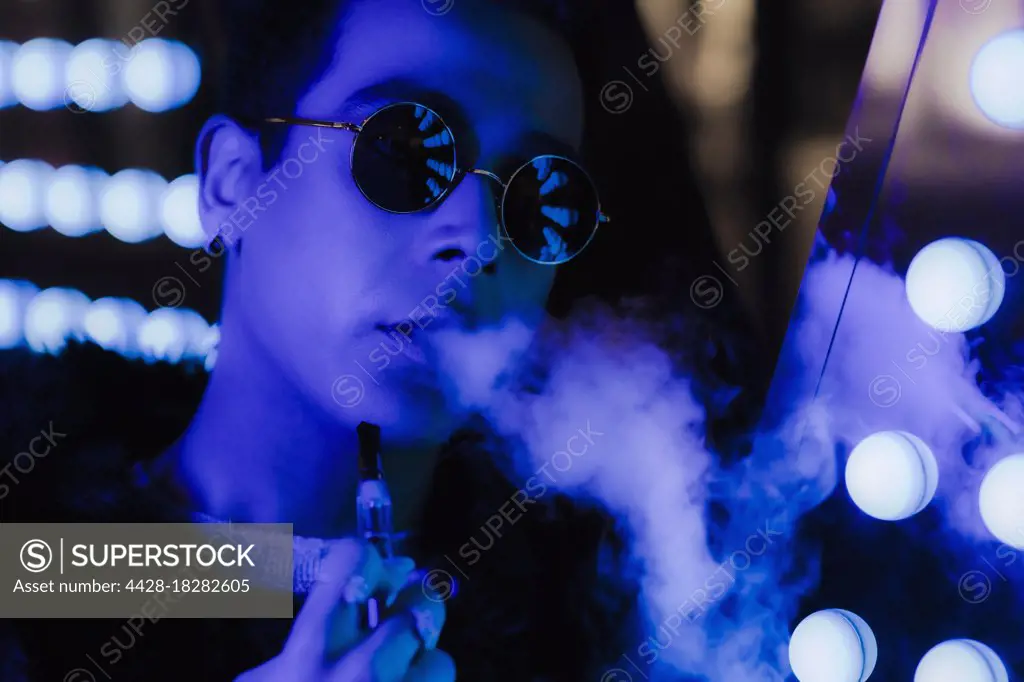 Portrait cool young man in sunglasses vaping in dark neon. nightclub