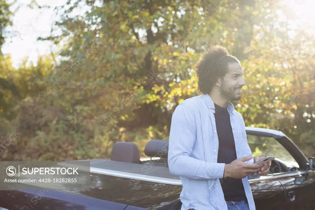 Young man with smart phone at convertible in sunny autumn park