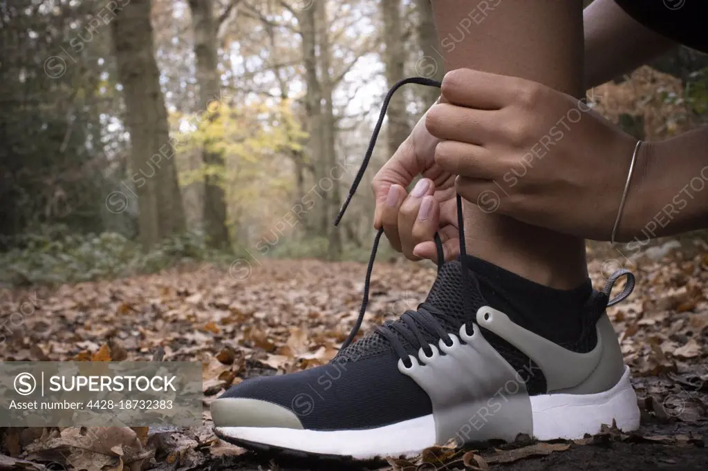 Close up female runner tying shoelace in autumn woods