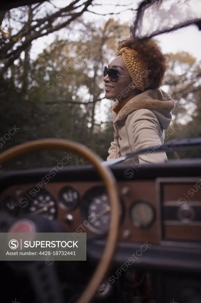 Happy young woman in sunglasses outside convertible in park