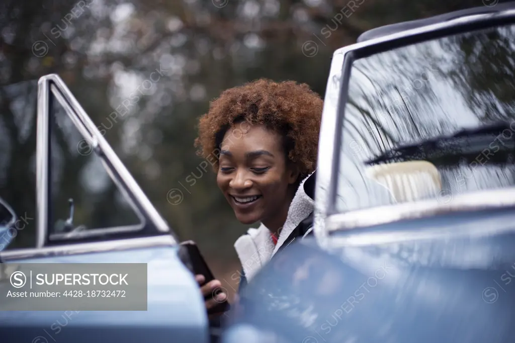 Happy young woman using smart phone at convertible