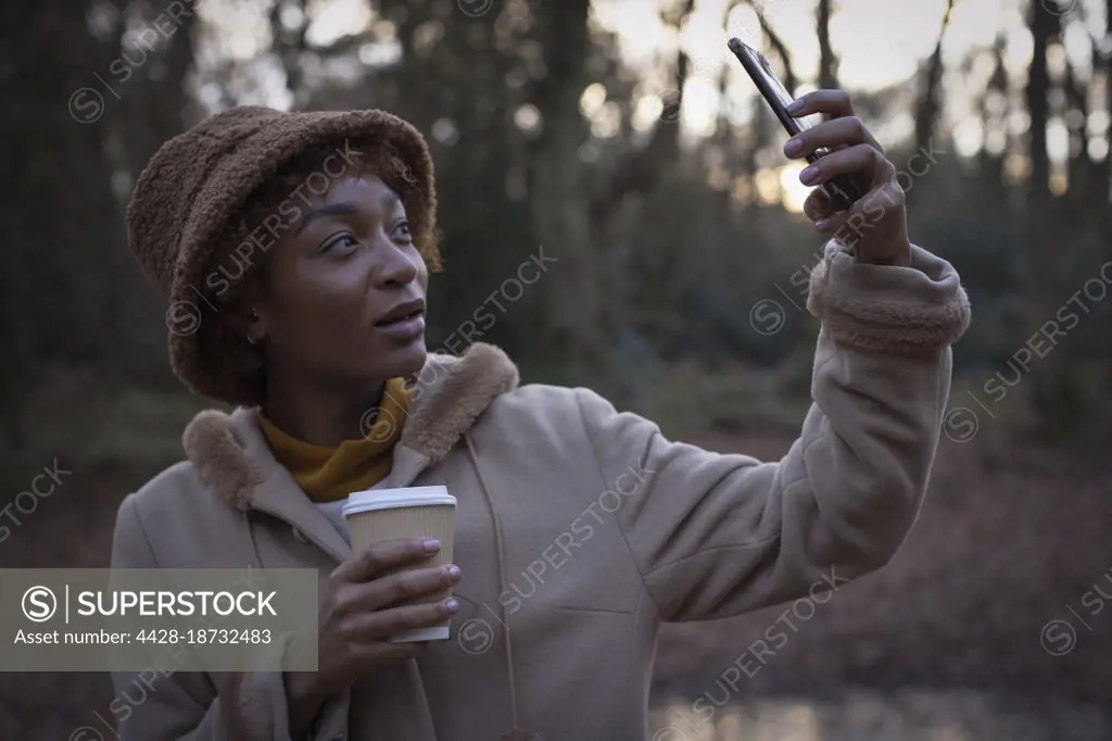 Young woman with coffee taking selfie in autumn park