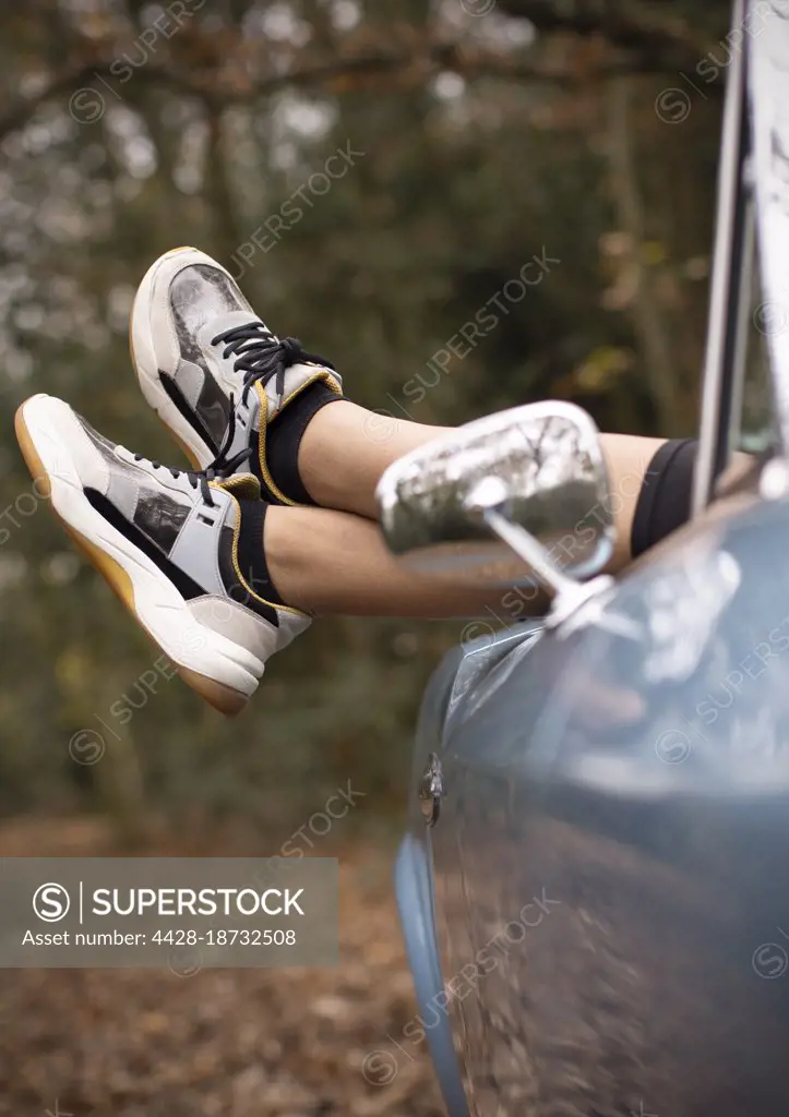 Carefree young woman with feet hanging out convertible in park