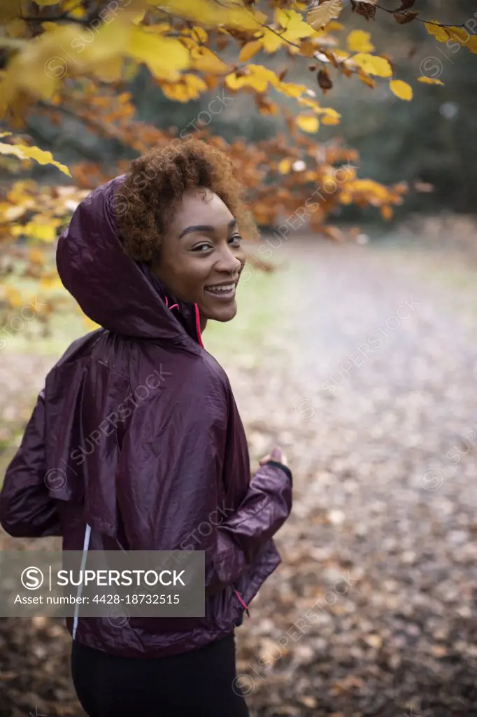 Portrait happy young woman jogging in autumn park