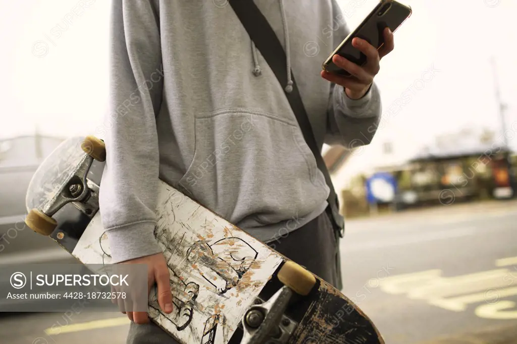 Close up teenage boy with skateboard and smart phone on street