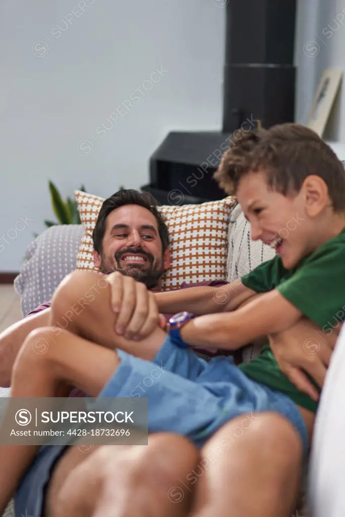 Happy father tickling son on living room sofa