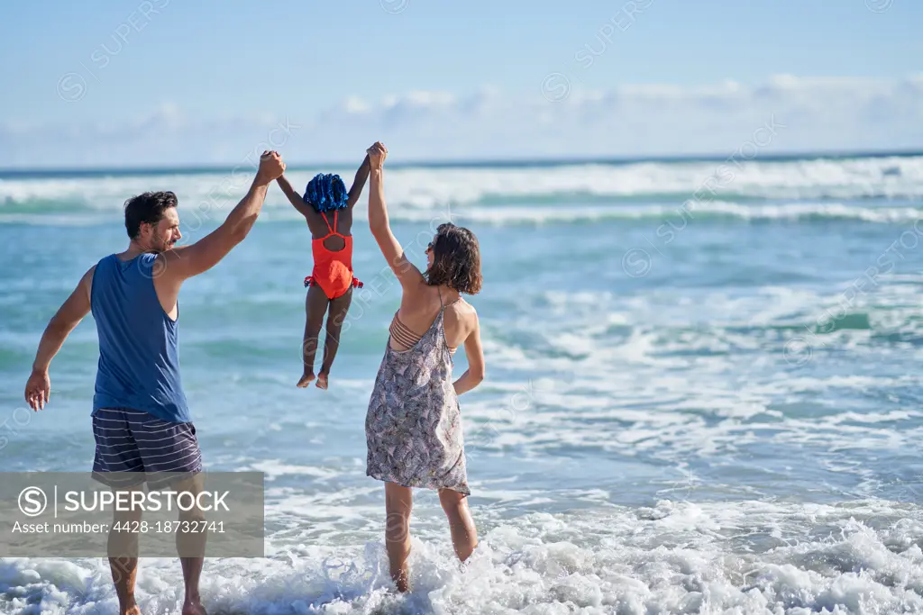 Parents lifting cute toddler daughter in sunny ocean surf