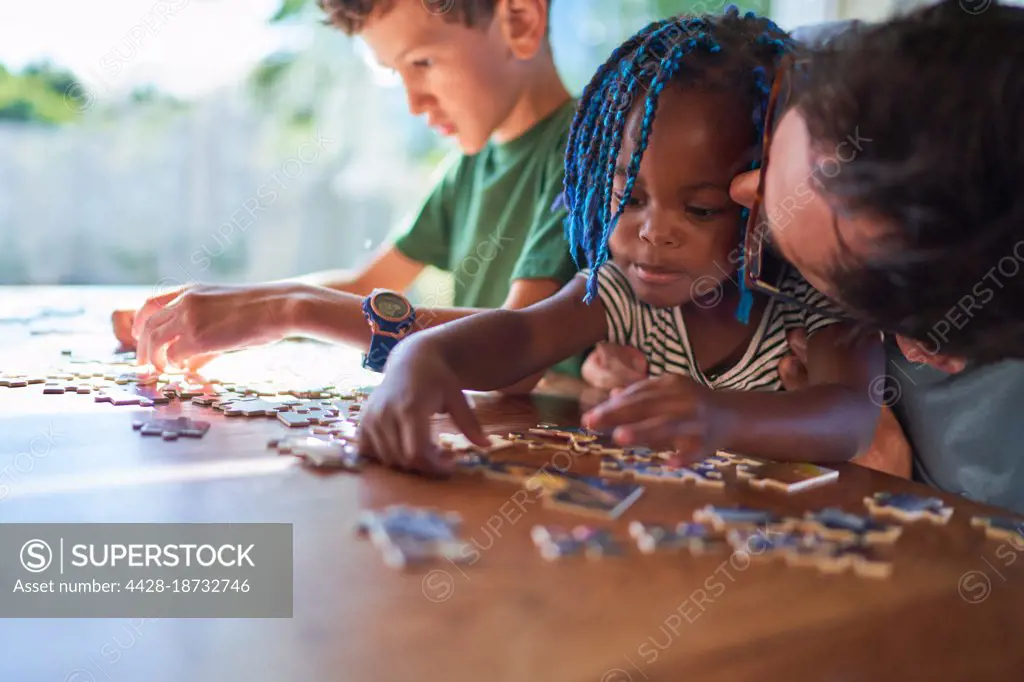 Father kissing cute toddler daughter assembling jigsaw puzzle